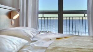 Habitación de hotel con cama, mesita de noche y vista al mar a través de la barandilla del balcón.