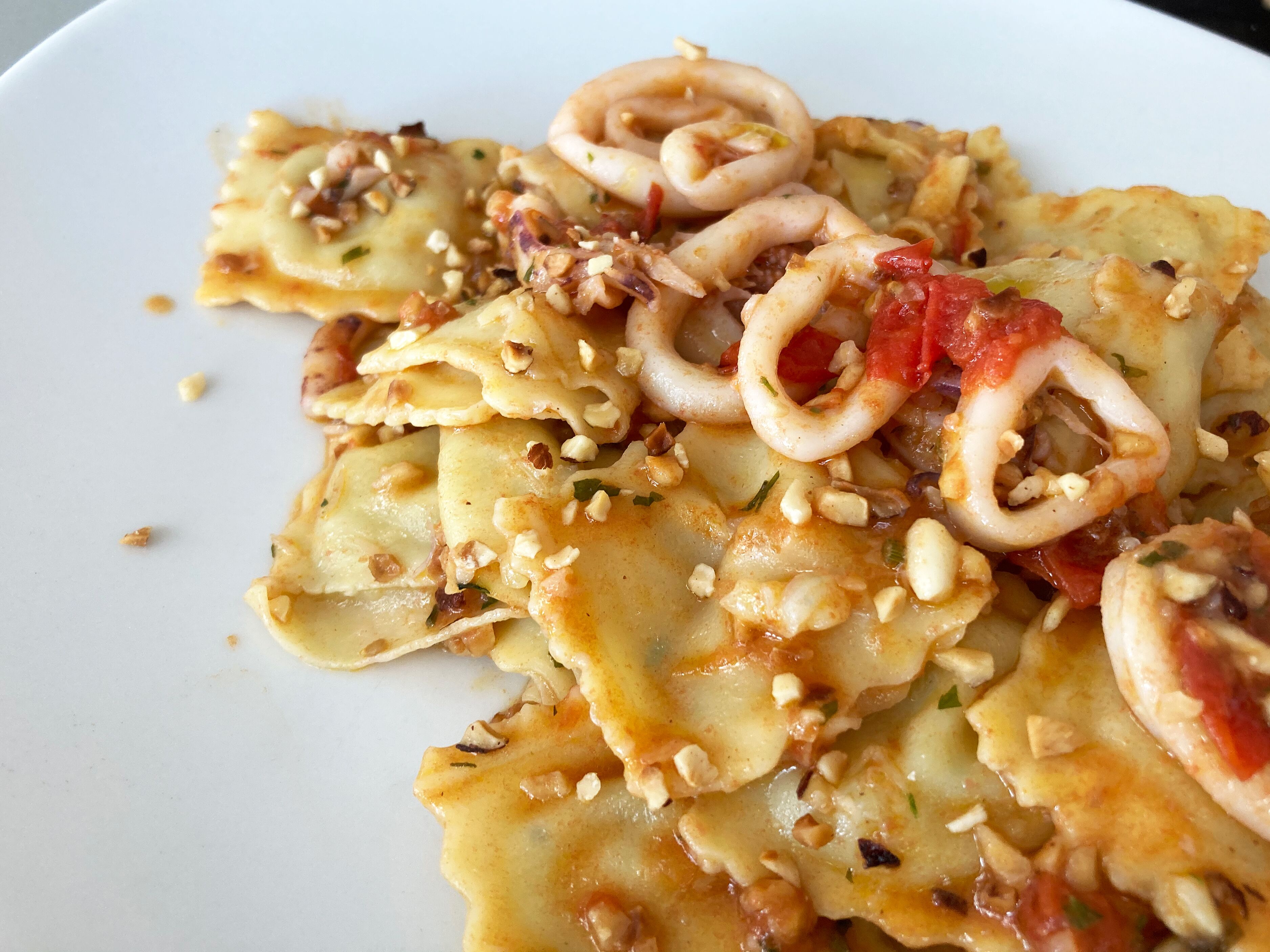 A plate of ravioli with squid rings and nuts.