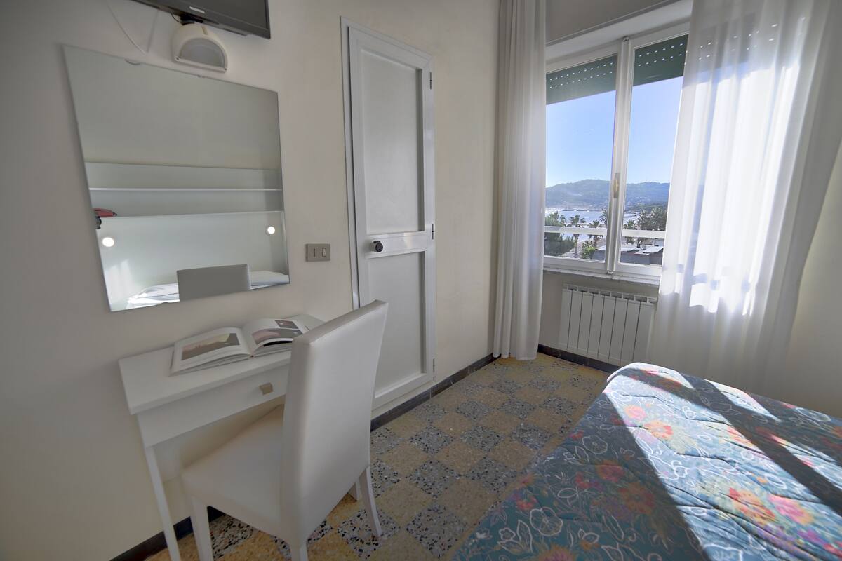 Een hotelkamer met een bed, een bureau, een stoel, een spiegel en een raam met uitzicht.