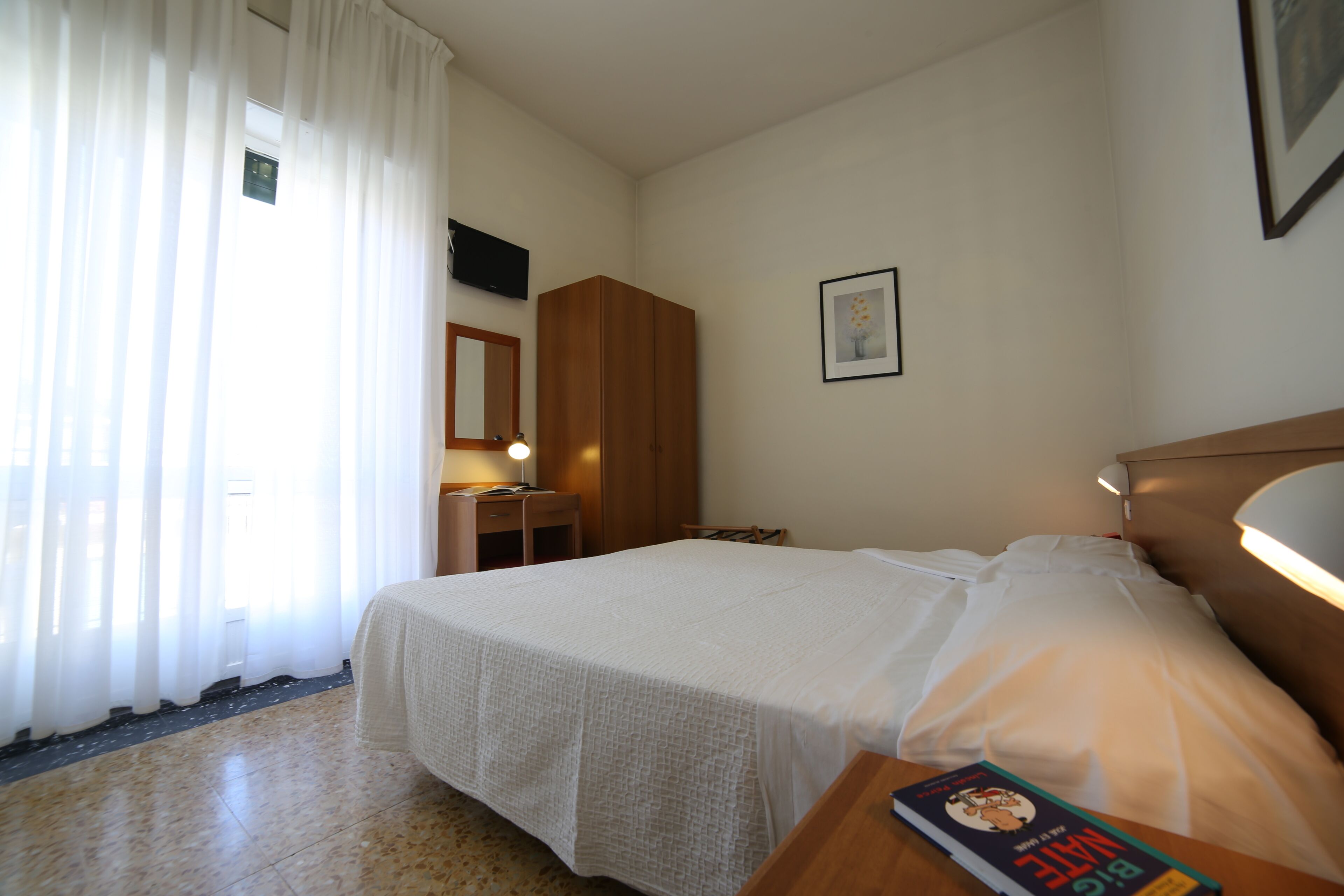 Une chambre d’hôtel bien rangée, avec un lit, une table de chevet, une lampe et un tableau encadré au mur.