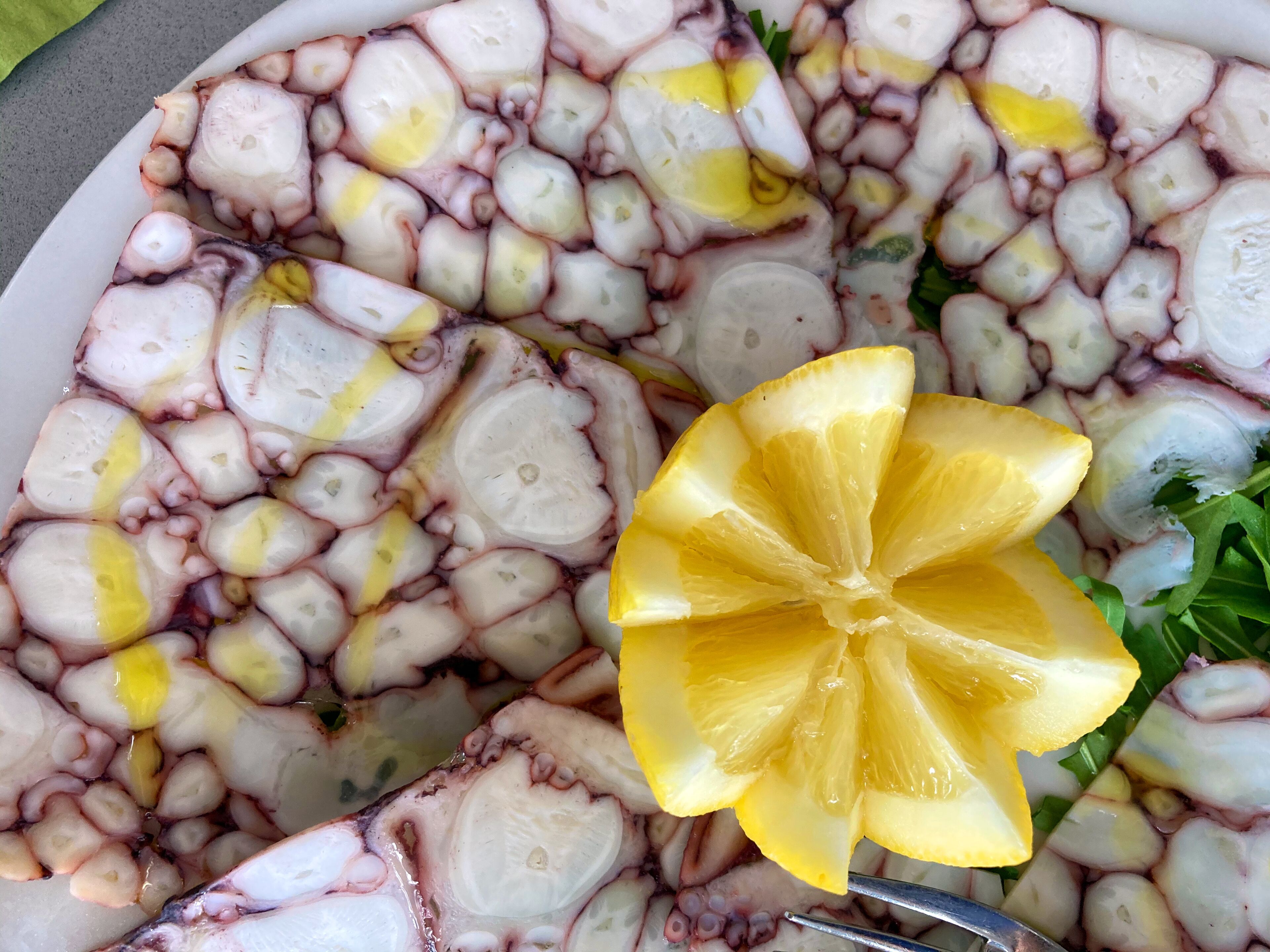 Une assiette de salade de poulpe, garnie de tranches de citron et de verdure.