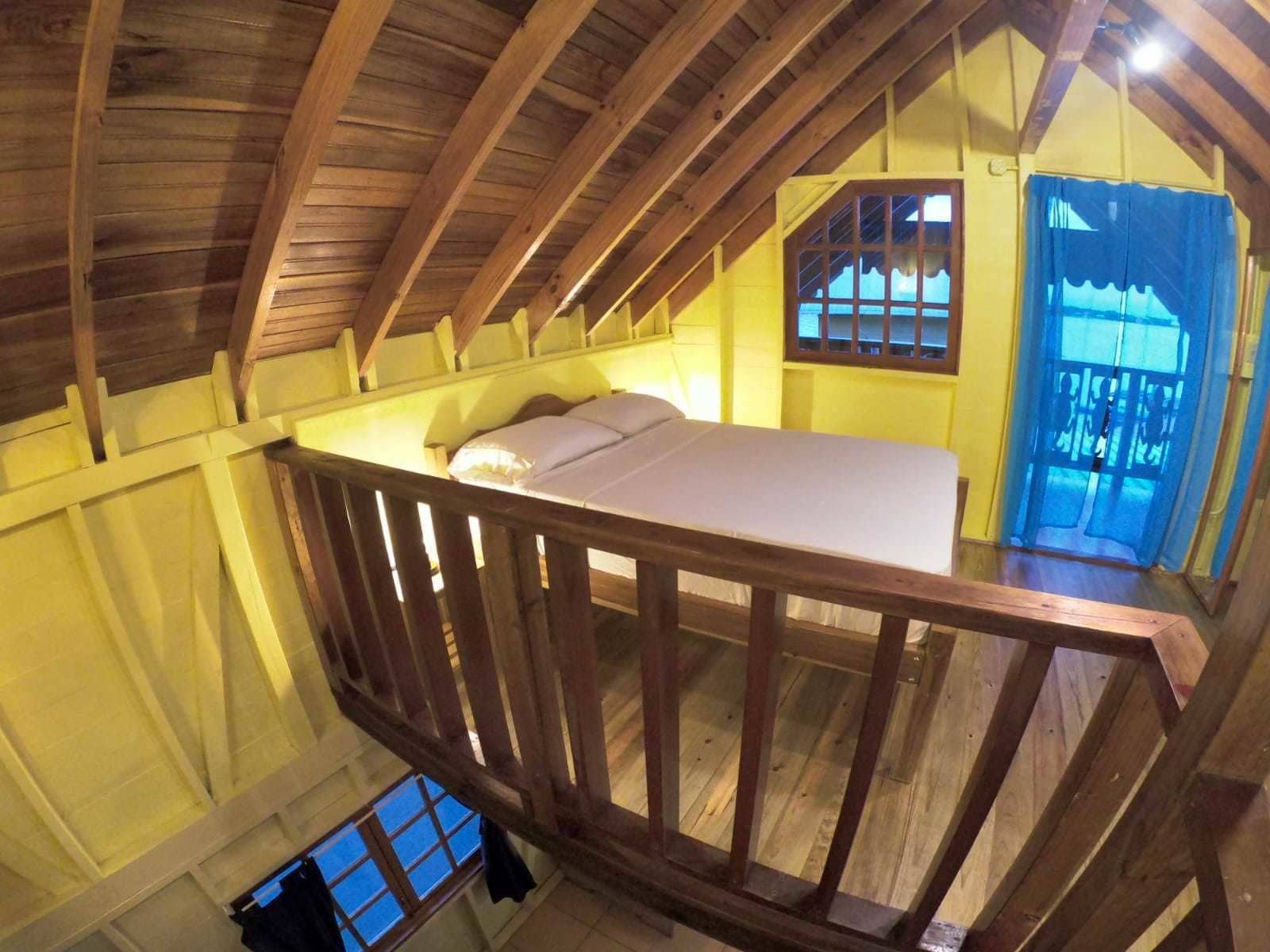 Ein Schlafzimmer unter der geneigten Dachschräge mit einem Holzbettkasten, einem Fenster mit Gitter und einer blauen Tür.