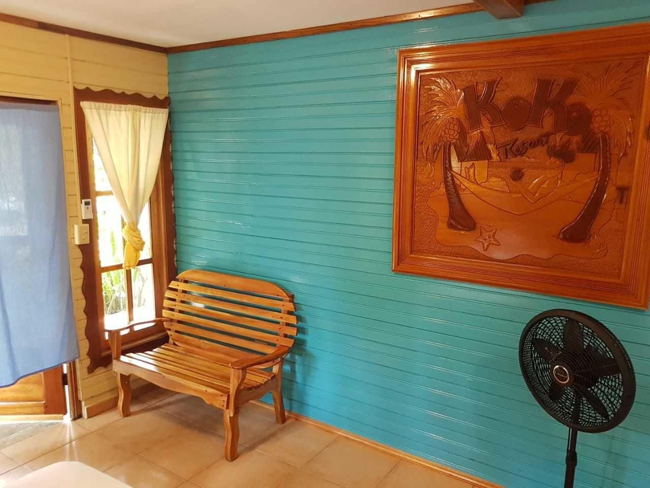 A room with a wooden bench, a fan, and a wall with a tropical mural.