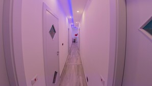 A narrow hallway with white walls and a wooden floor, leading to a room with a red object on a table. - Civico 364 (Naples)