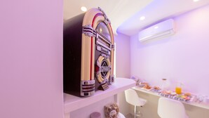 A retro-styled jukebox on a shelf, a breakfast bar with chairs, and an air conditioning unit on the wall. - Civico 364 (Naples)