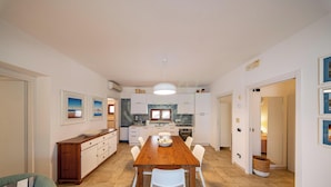 A modern kitchen with white cabinets, a wooden dining table, and a hanging light fixture.