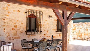 An outdoor dining area with a stone wall, metal chairs, a table, and a window with a metal grill.