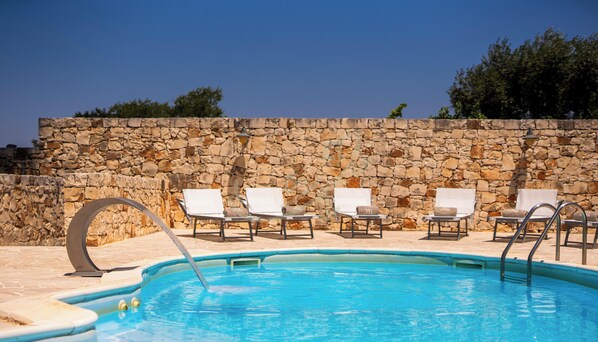 A swimming pool with lounge chairs and a stone wall. - TD Villa Luna Trulli with Large Pool (Castellana Grotte)