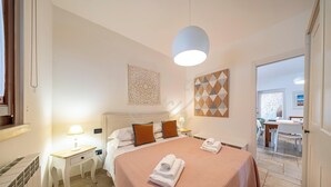 A hotel room with a bed, bedside tables, a lamp, a decorative wall piece, and a geometric wall art.