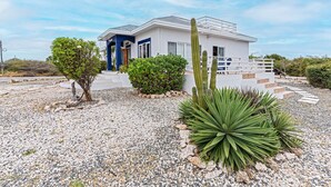 A modern house with a white exterior, a blue door, and a gravel driveway. - Villa Amarc: Family Fun, Kite Surf, Balcony View minutes to Rodgers/Baby Beach! (San Nicolas)