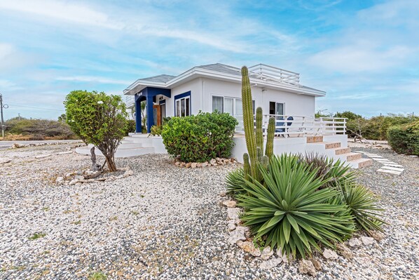A modern house with a white exterior, a blue door, and a gravel driveway.