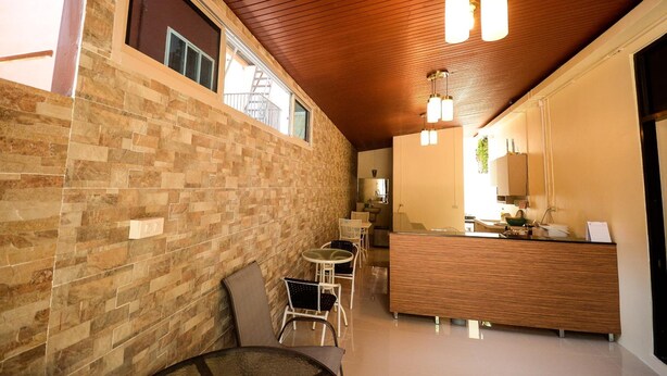 A modern kitchen with a wooden countertop and a built-in oven. There is a dining area with a table and chairs, and a brick wall on one side. - U-need Guesthouse (Bangkok)