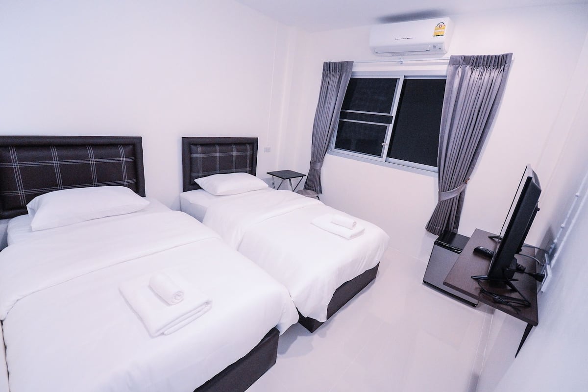 A hotel room with two beds, a flat-screen TV, an air conditioner, and a window with curtains.