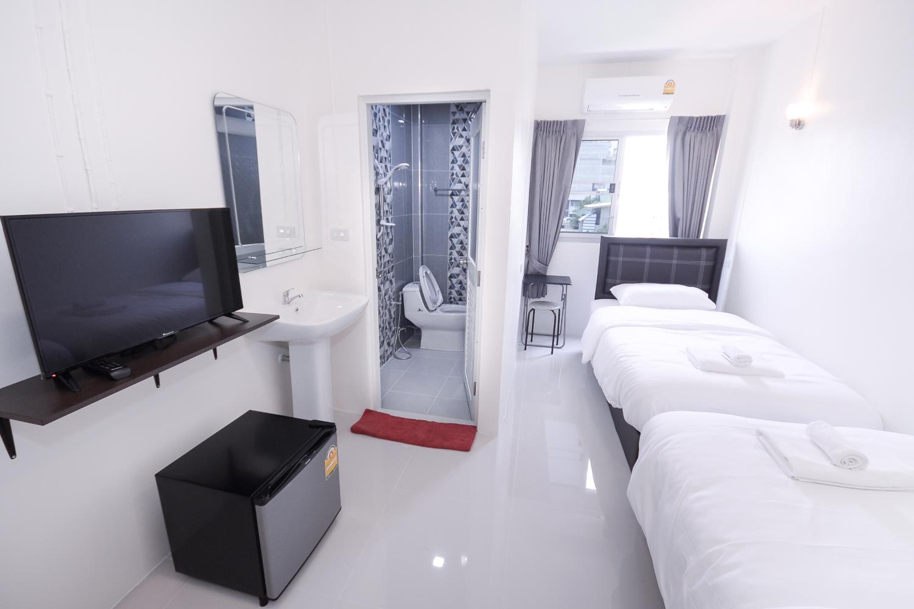 A hotel room with a TV, a small sink, a red rug, two beds, and a view of the city through a window.