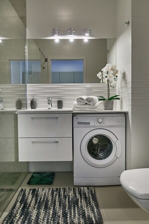 A modern bathroom with a built-in washing machine, a toilet, a sink with a mirror, and a potted orchid. - Praga Elegant Studio (Warsaw)