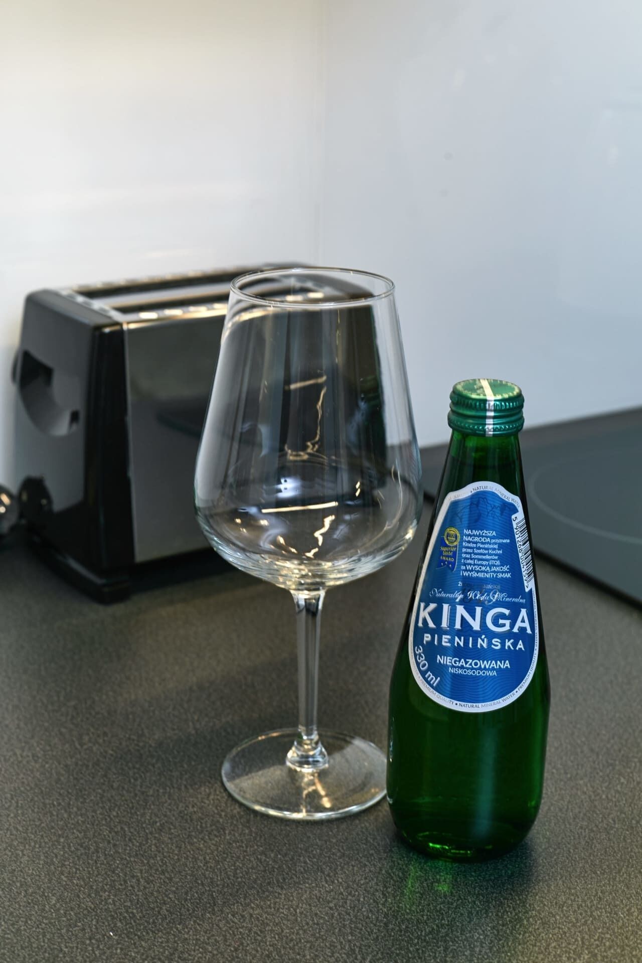 A clear glass of water next to a bottle of Kinga Pienińska mineral water on a kitchen counter.