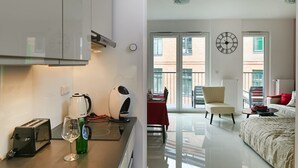 A modern kitchen with a toaster, kettle, and wine glass, a dining area with a red table, and a bedroom with a bed and a chair. - Praga Elegant Studio (Warsaw)