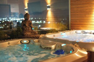 A hot tub area with a Buddha statue, a view of the cityscape, and a wooden wall.