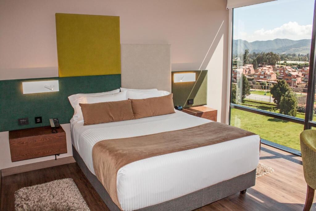 Un dormitorio moderno con una cama grande, vistas de la ciudad y una pared verde decorativa.