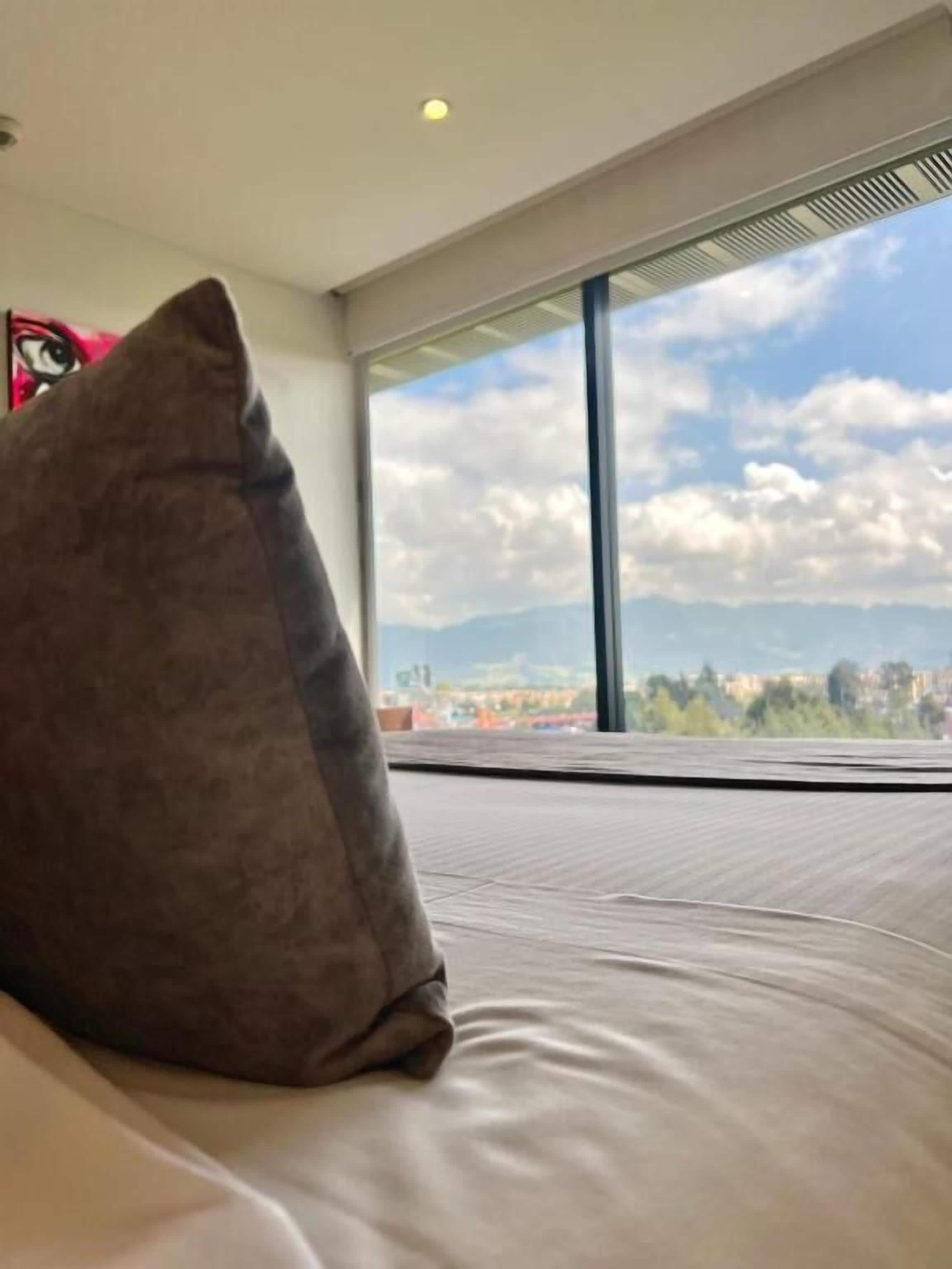 A bedroom with a large window offering a cityscape view.