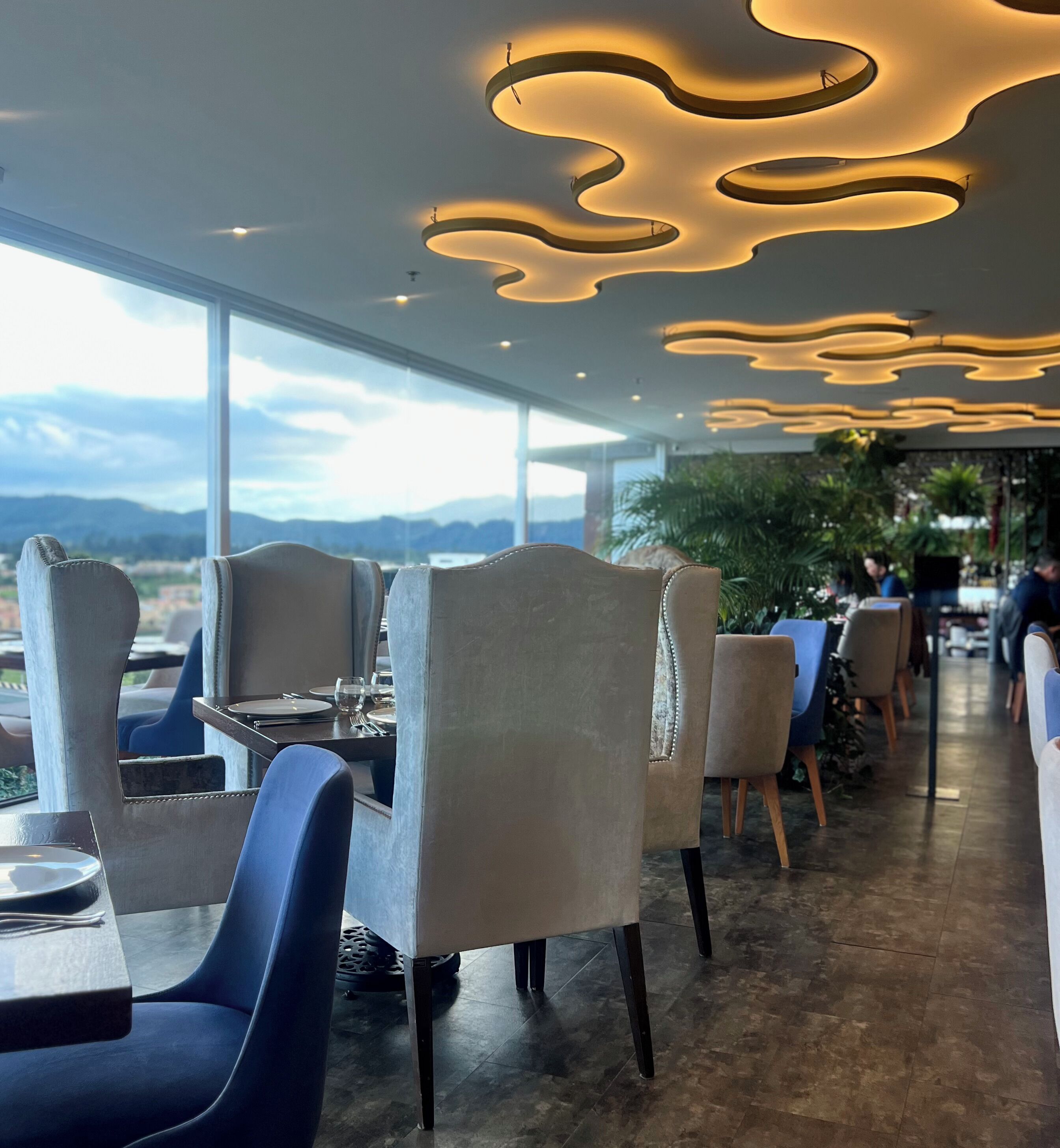 Un ristorante con arredamento moderno, caratterizzato da luci a soffitto curve e vista sulle montagne attraverso ampie finestre.