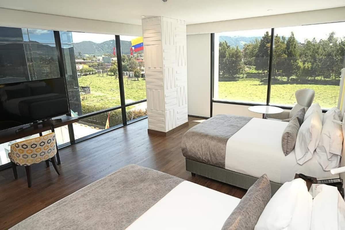 Un hotel moderno con una cama grande, un televisor y vistas a un paisaje verde a través de amplias ventanas.