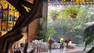 Relax in a tranquil atmosphere surrounded by lush greenery and a rustic tree trunk, with a bar area offering a selection of fine spirits.