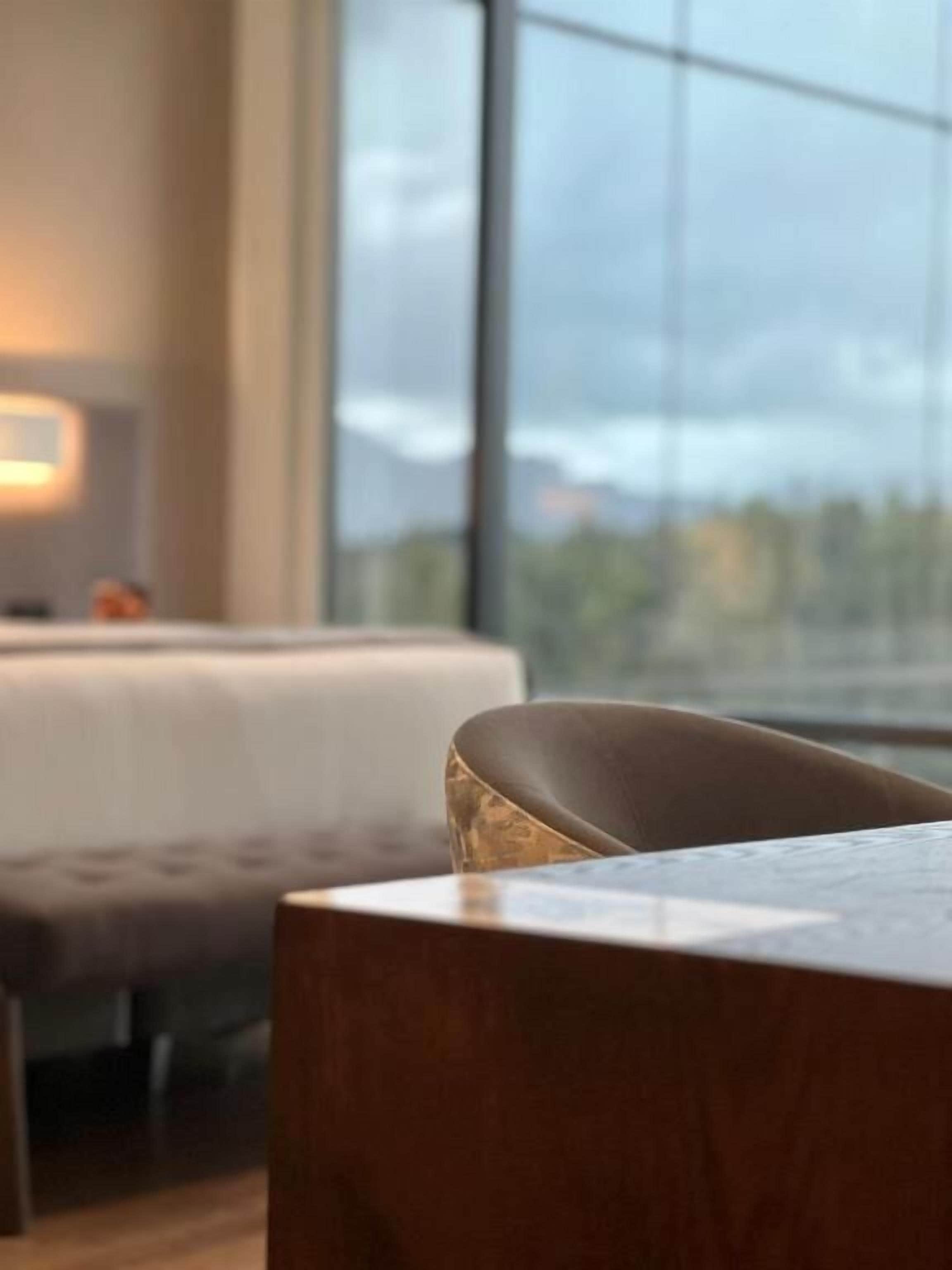 A modern hotel room with a large window, a wooden table, and a sofa.