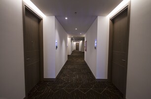 A hotel hallway with dark patterned carpet, wooden doors, and recessed lighting.