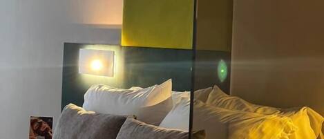 A neatly made bed with pillows, a bedside table, and a wall-mounted light fixture.