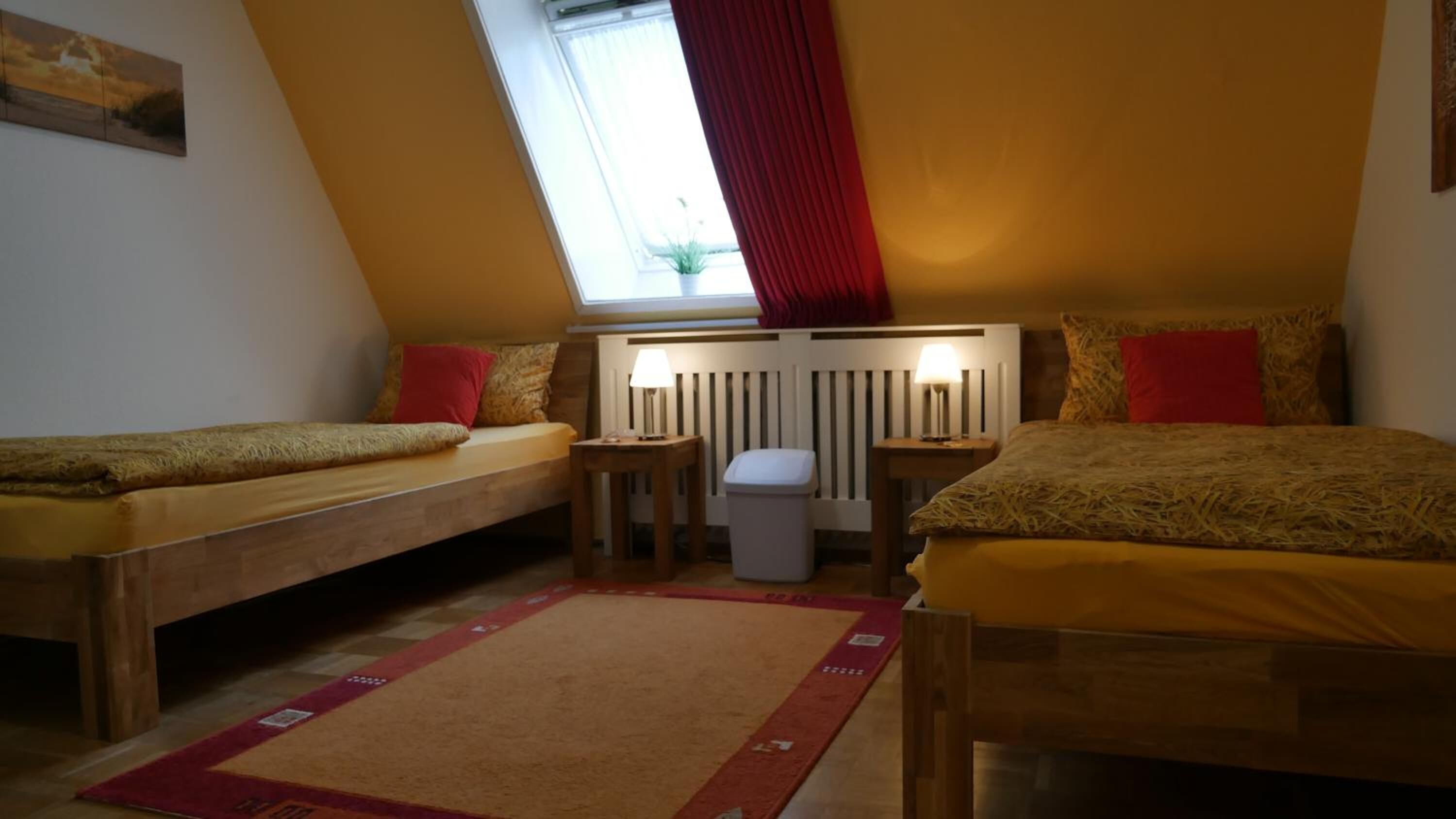 A cozy room with two single beds, a small table, a waste bin, and a radiator.