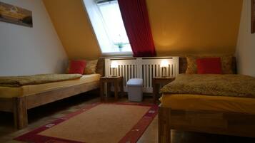 A cozy room with two single beds, a small table, a waste bin, and a radiator.