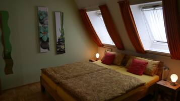 Een slaapkamer met een bed, twee wanddecoraties, een raam met gordijnen en een nachtkastje met een lamp.