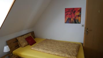 A small, triangular room with a bed, a red pillow, and a painting on the wall.