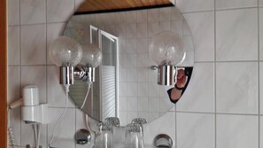 A bathroom with a large mirror, two wall-mounted light fixtures, a hairdryer, and a toothbrush. - Altes Farmhaus (Lienen)