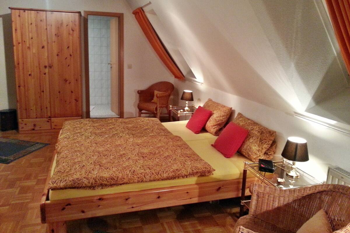 Un dormitorio con una cama de madera, una silla, una mesita de noche y una ventana con cortinas.