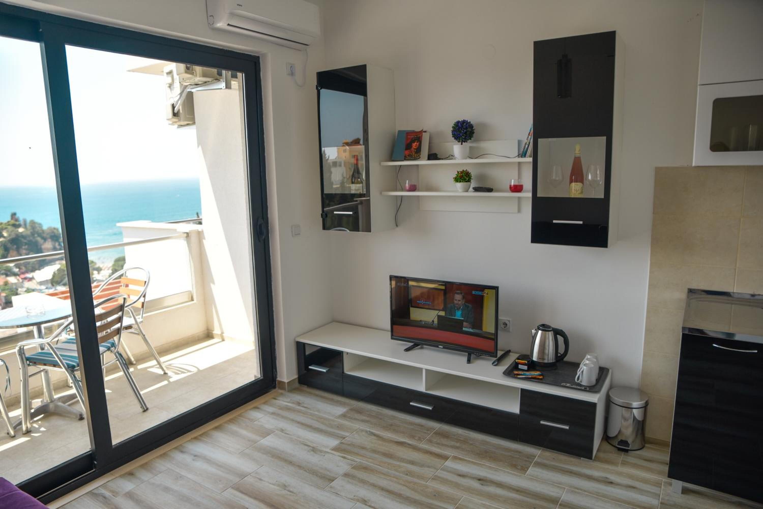 A modern living room with a TV, shelves, and a view of the sea.