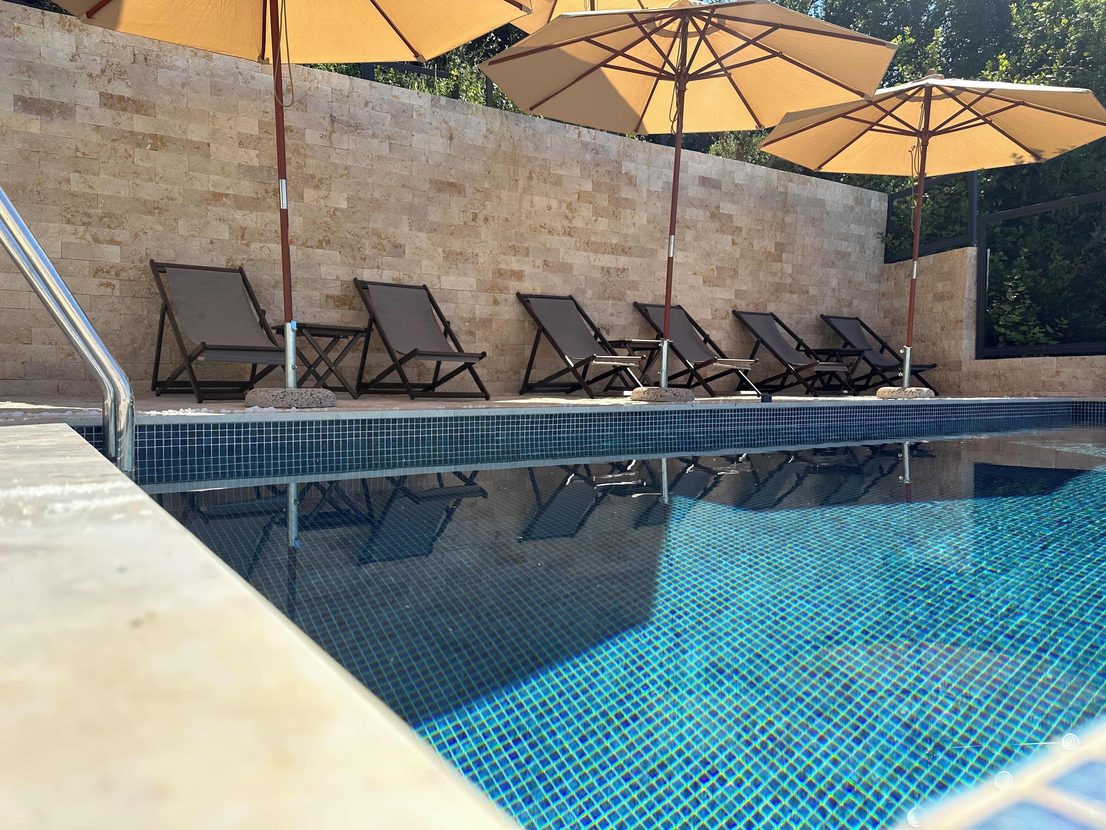A swimming pool with tiled edges, lounge chairs, and umbrellas.