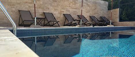 A swimming pool with tiled edges, lounge chairs, and umbrellas.
