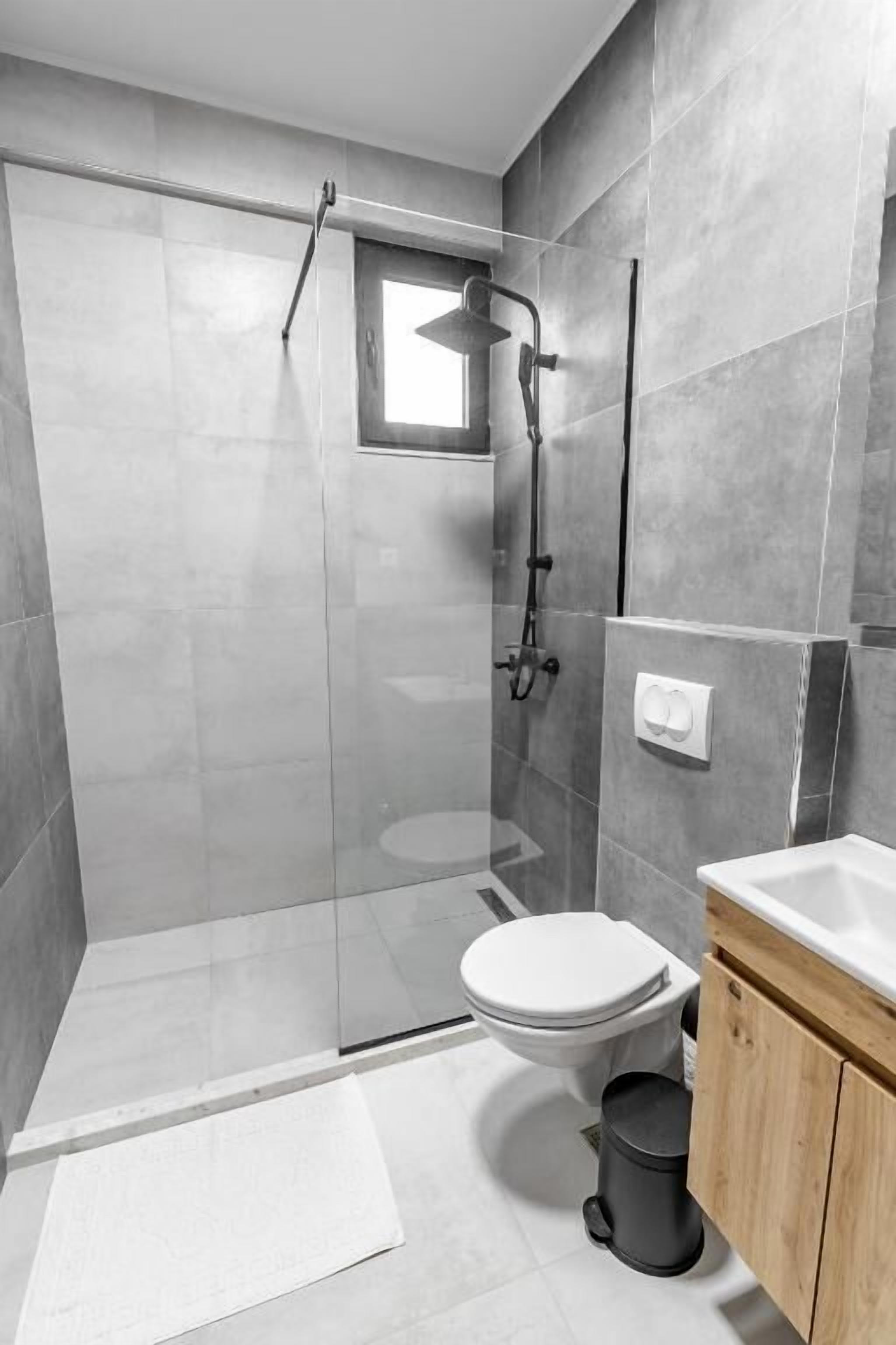 Un baño moderno con ducha envuelta en vidrio, inodoro y lavabo con armarios de madera.