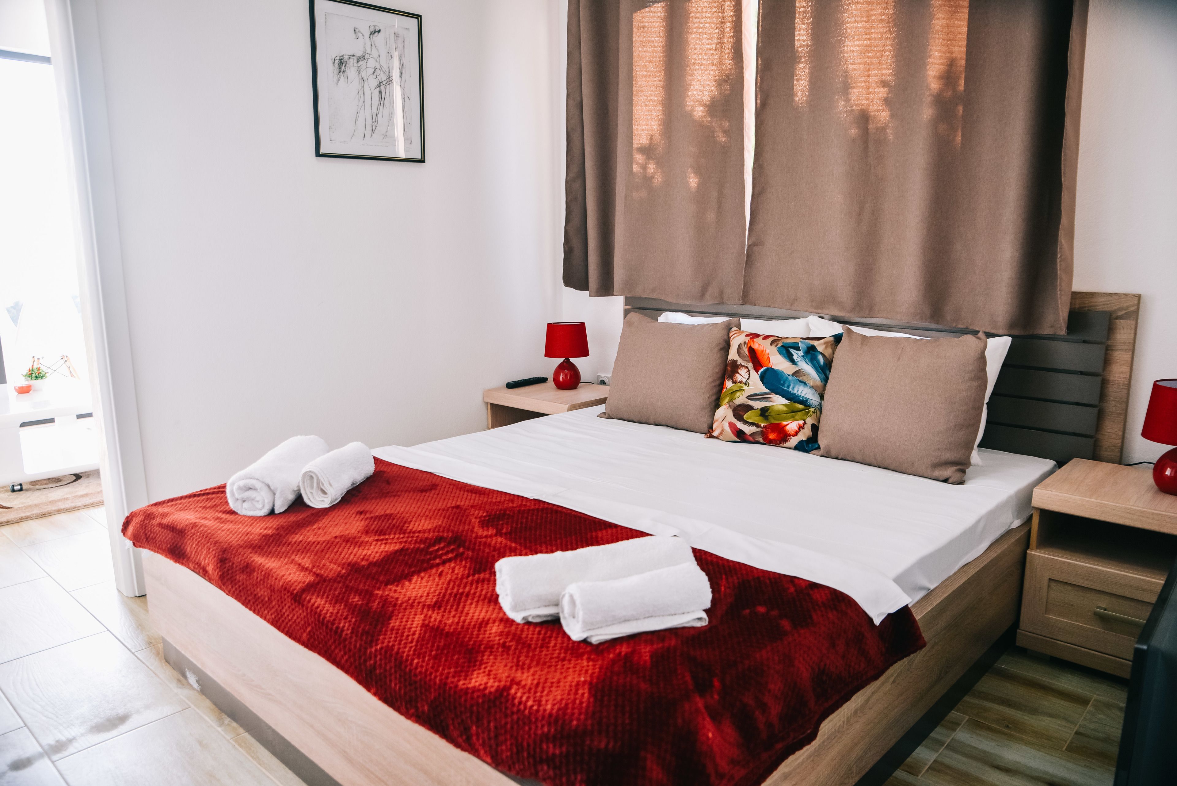 A neatly made bed with a red blanket and white towels, a wooden headboard, and a red lamp on each side.