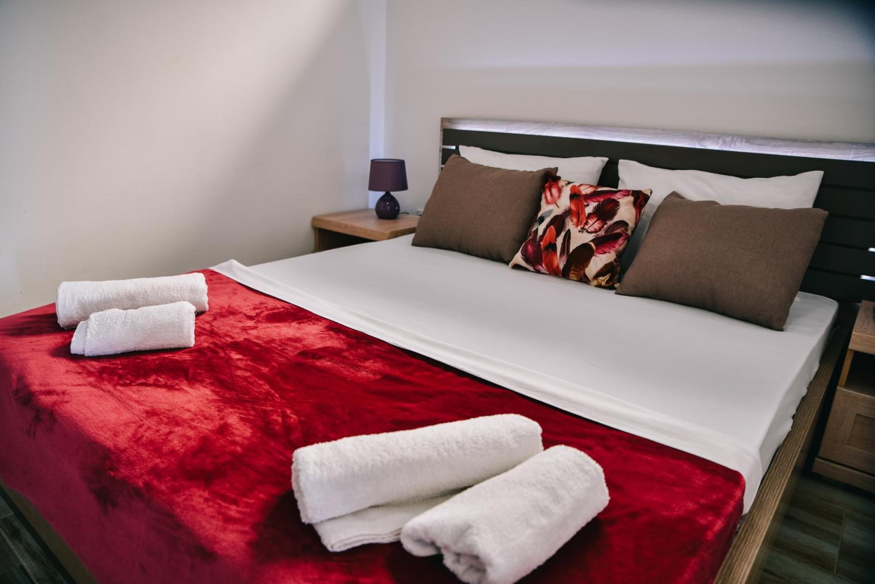 A neatly made bed with a red blanket and white pillows, a bedside lamp, and a nightstand.