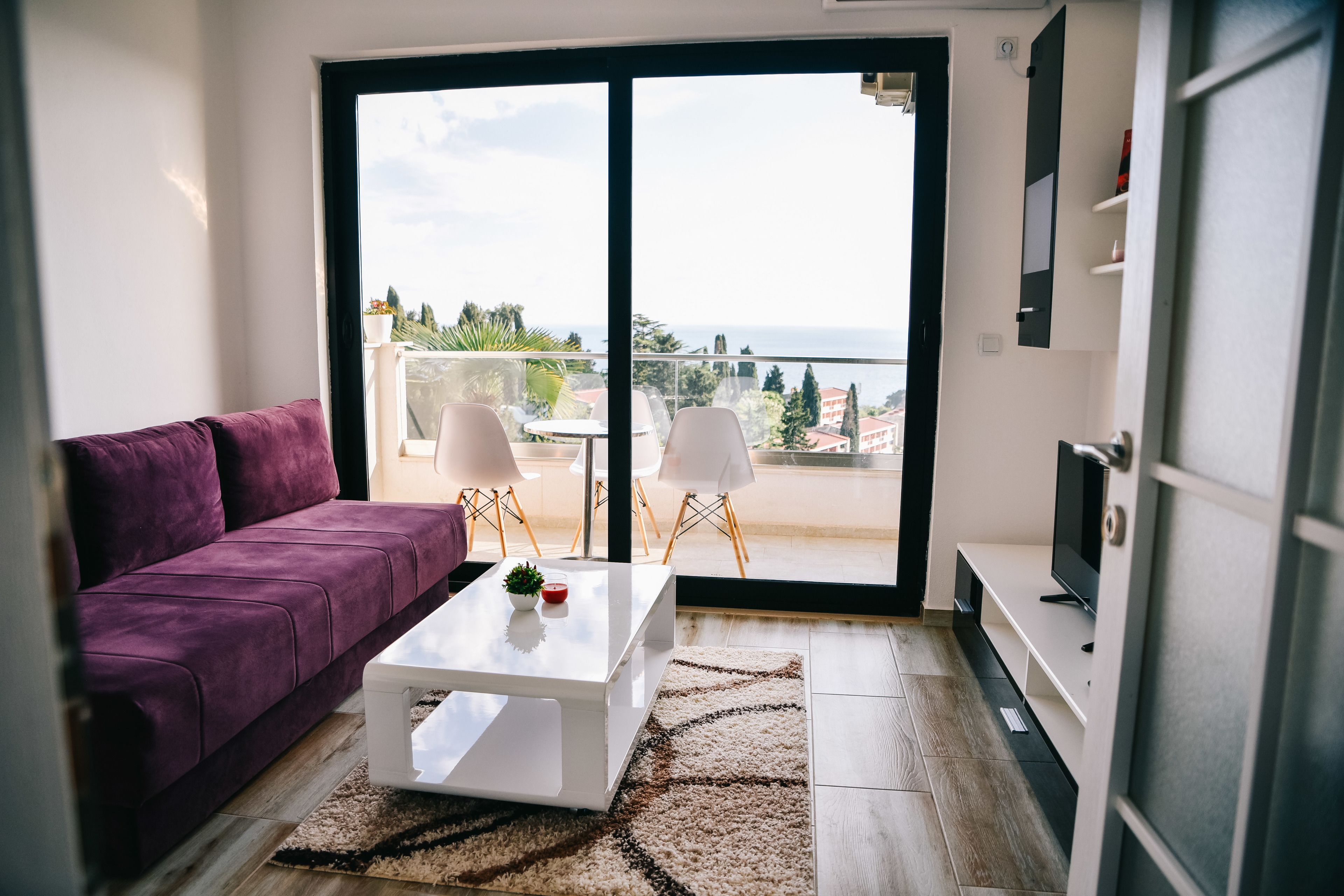 Un salon moderne avec un canapé violet, une table basse blanche et un balcon offrant une vue agréable.
