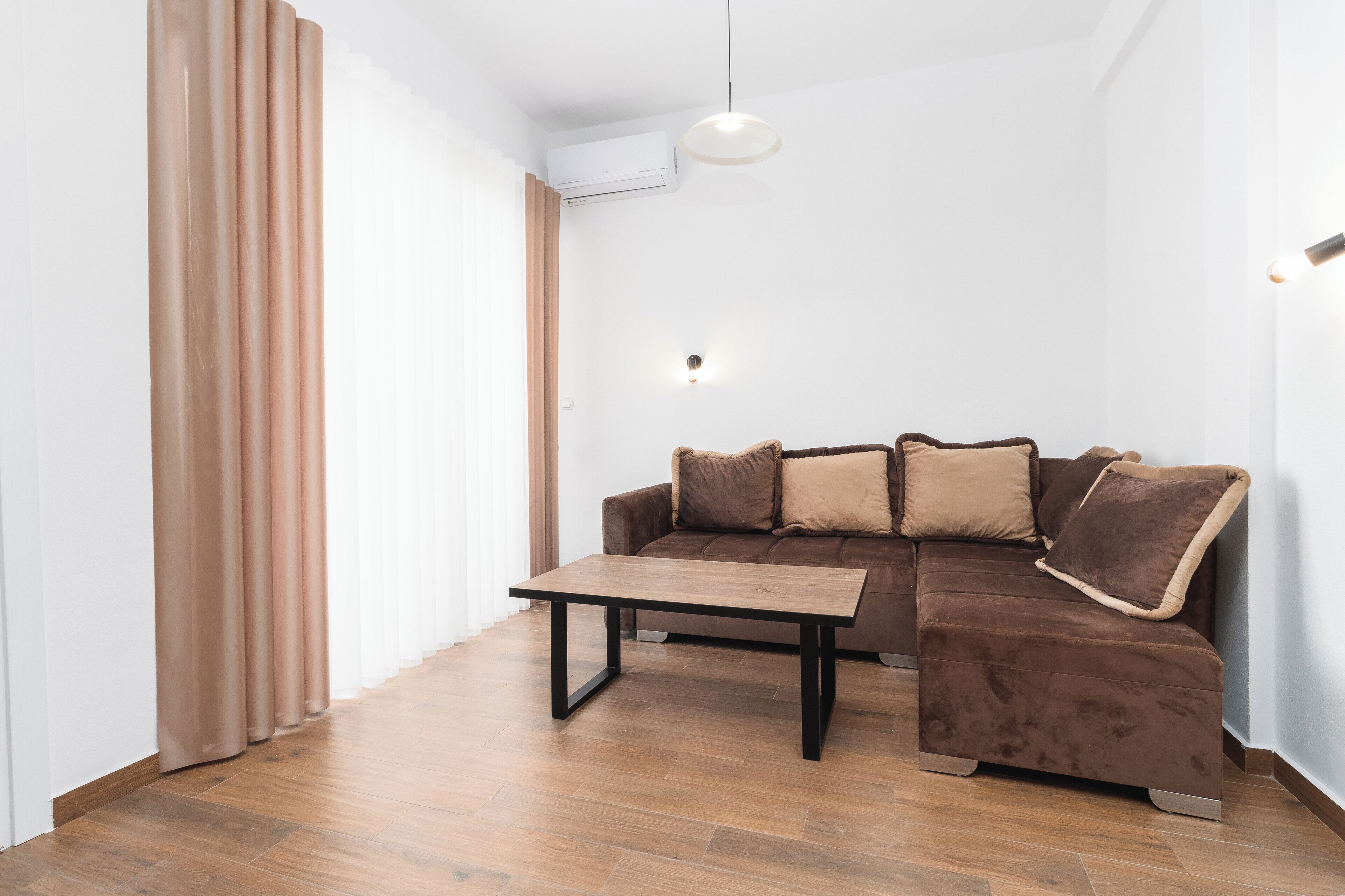 Uma sala de estar moderna com um sofá marrom, uma mesa de centro de madeira e uma luminária no teto.