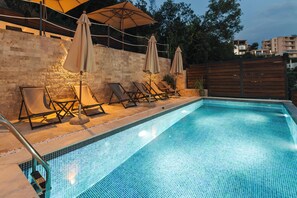A swimming pool with lounge chairs and umbrellas, surrounded by a stone wall and wooden fence. - Casa Bianca (Ulcinj)