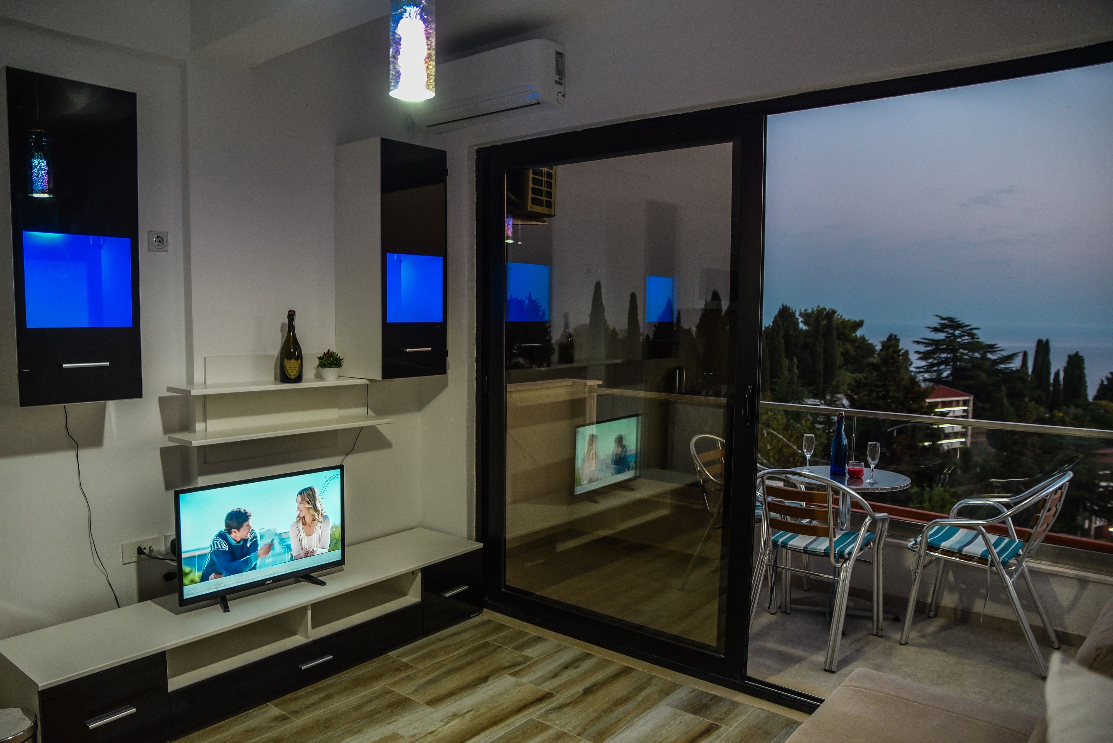 Een moderne woonkamer met een flatscreen televisie, een fles wijn en een balkon met zitplaatsen buiten.