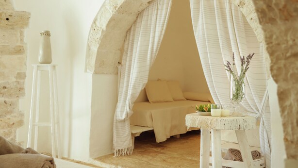 Um quarto aconchegante com cama, uma mesinha com um vaso e uma escada encostada em uma parede de pedra.