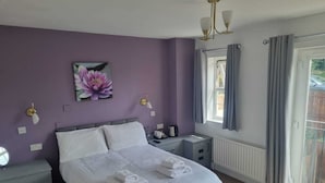 A bedroom with a bed, bedside tables, a nightstand, a window with curtains, and a wall-mounted light fixture. - The Moorings (Chester-le-Street)