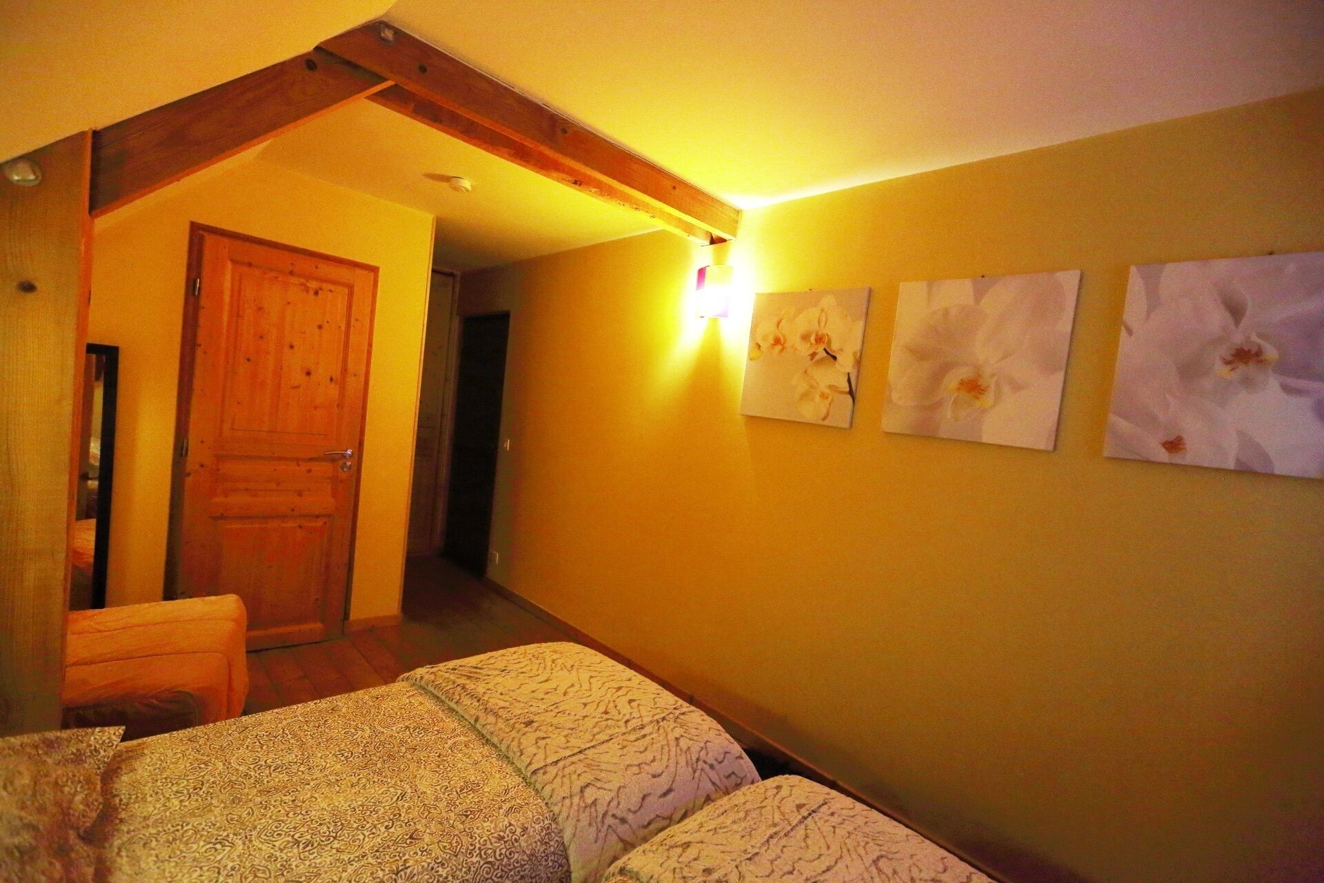 A room with a wooden door, a bed with patterned bedding, and three wall-mounted orchid paintings.