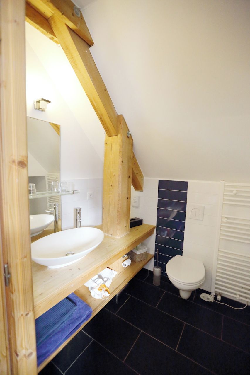 A bathroom with a wooden vanity, a white sink, a mirror, a toilet, and a tiled wall.